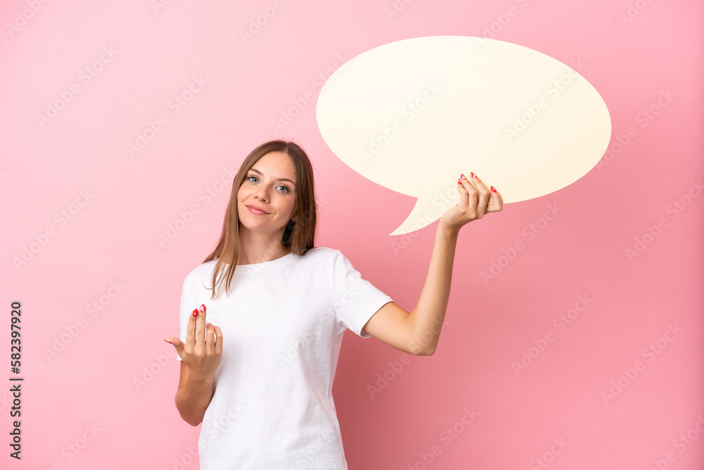 Young Lithuanian woman isolated on pink background holding an empty speech bubble and doing coming gesture Young Lithuanian woman isolated on pink background holding an empty speech bubble and doing coming gesture