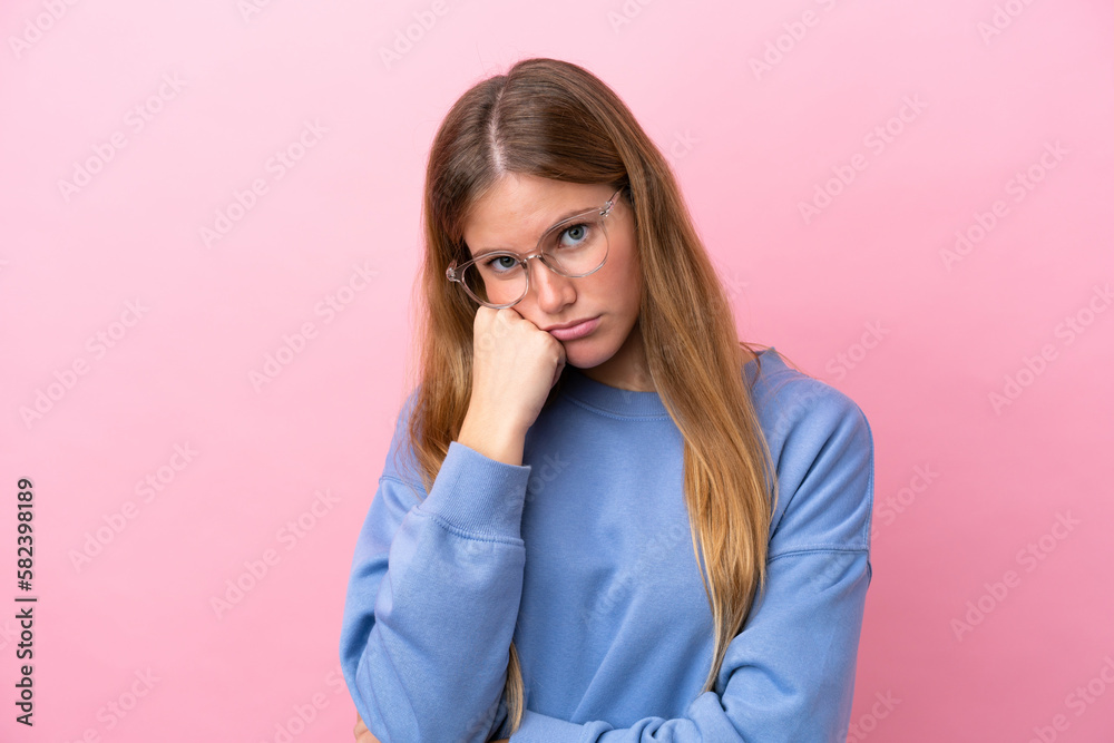 Young blonde woman isolated on pink background With glasses and with sad expression