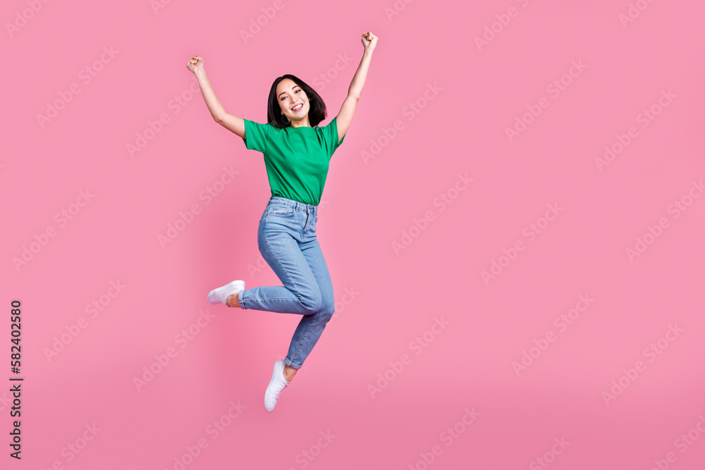 Full length photo of satisfied girl dressed green t-shirt denim trousers jumping celebrating winning isolated on pink color background