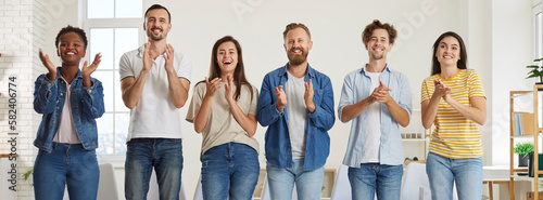 Team of happy diverse people clapping hands. Group of cheerful  joyful men and women in casual T shirts and jeans standing in office  smiling and applauding speaker for good presentation