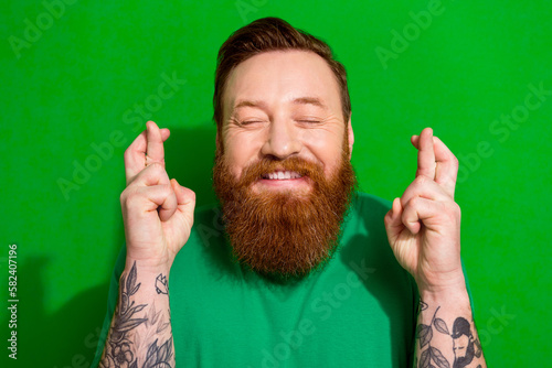 Photo of funky excited guy dressed t-shirt smiling fingers crossed closed eyes isolated green color background