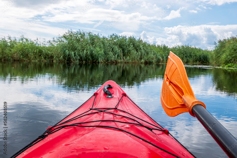Kayaker point of view. Red kayak bow with a view on the river and rushes. River kayaking concept. Active vacations in wild nature.