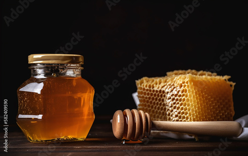 Square honey jar beside a full honeycomb with a wooden dipper on dark wood.