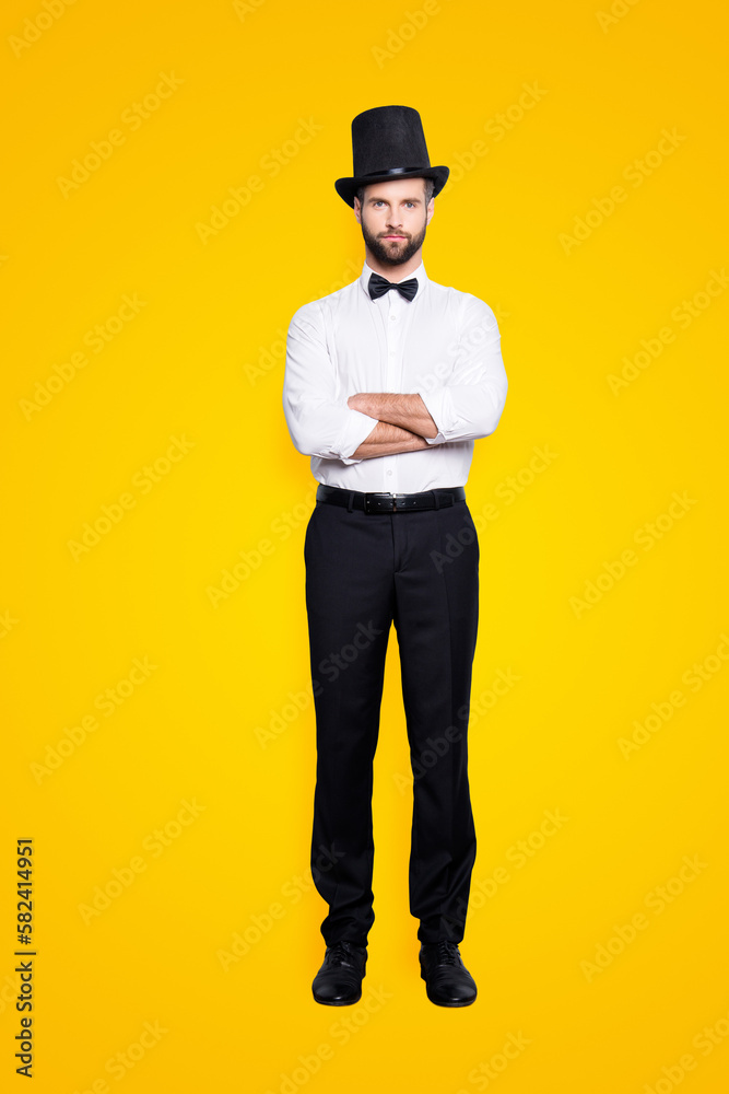 Full size fullbody portrait of stylish attractive magician in tophat having his arms crossed, looking at camera, isolated on grey background