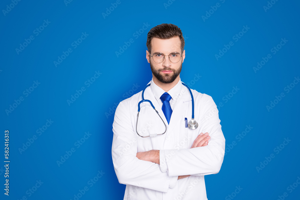Portrait of attractive stylish doc with stubble in white lab coat, tie and stethoscope on his neck, having his arms crossed, looking at camera, isolated on grey background