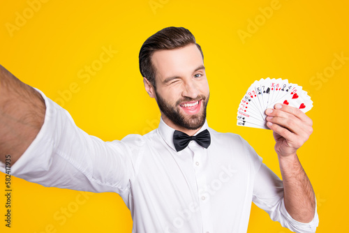 Self portrait of playful flirting croupier shooting selfie on front camera winking with eye demostrate present set of cards, isolated on grey background, having leisure video-call photo