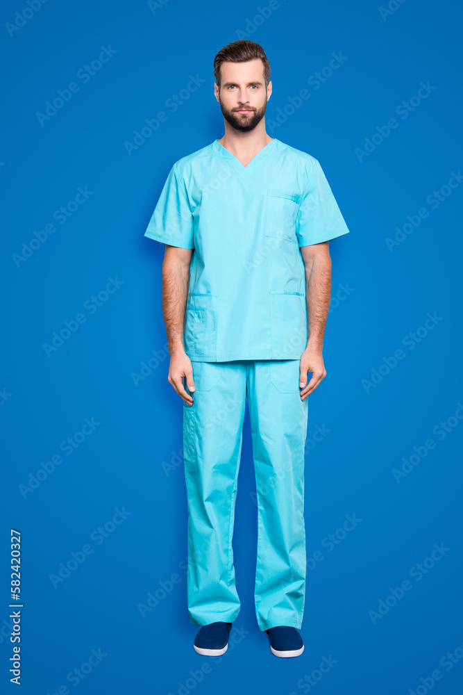 Full size body portrait of virile harsh man with bristle, hairstyle in blue lab suit, looking at camera, isolated on grey background Full size body portrait of virile harsh man with bristle, hairstyle in blue lab suit, looking at camera, isolated on grey background