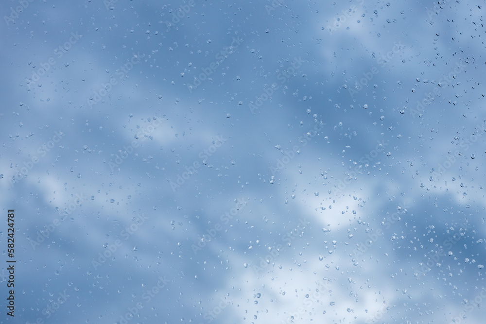 Raindrops on window pane on blue sky, weather concept 