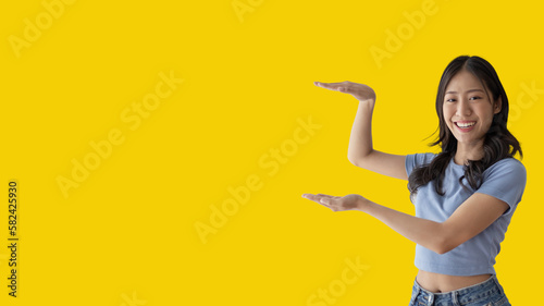 Asian woman with holding copyspace imaginary on the palm to insert an ad  Showing copyspace pointing  Showing her hand to present something on yellow background.