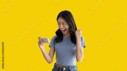Asian woman playing games on mobile phone and wearing headphones having fun, Play games on the sofa in the living room on weekends, Resting at home, Comfort zone, Touch screen mobile phone.