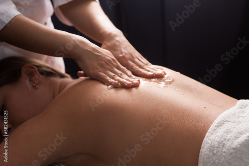 masseur doing back massage with honey in dark room