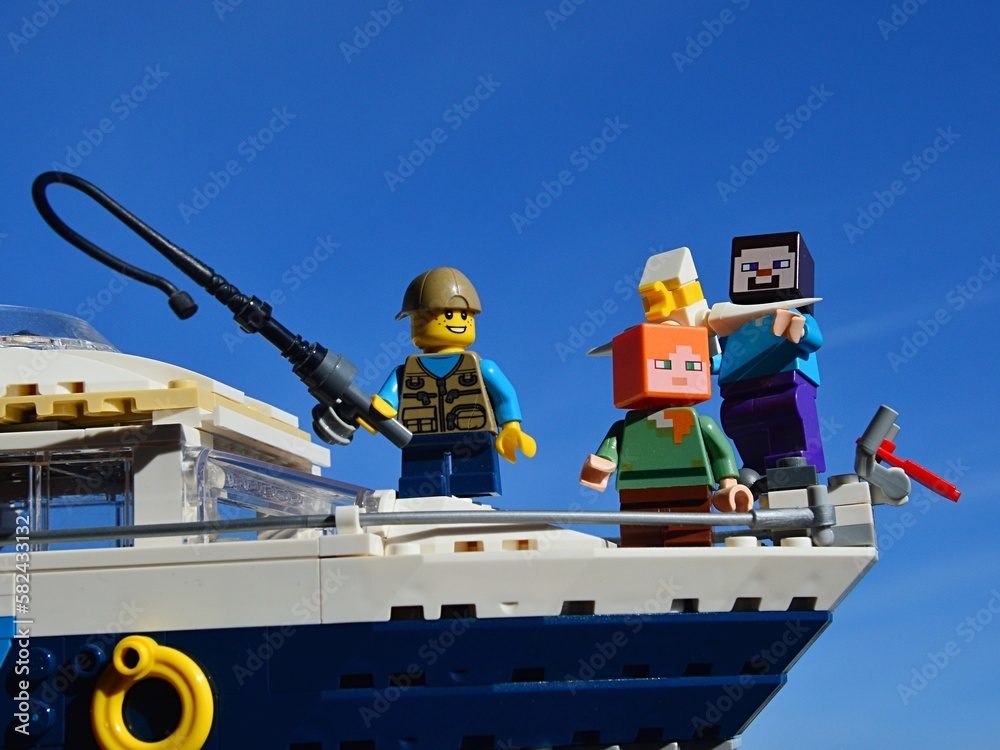 Fototapeta premium LEGO Minecraft Steve and Alex on yacht with a boy with fishing pole from LEGO Creator series, enjoying sunny day on sea. Seagull is captured in hands of smiling Steve.