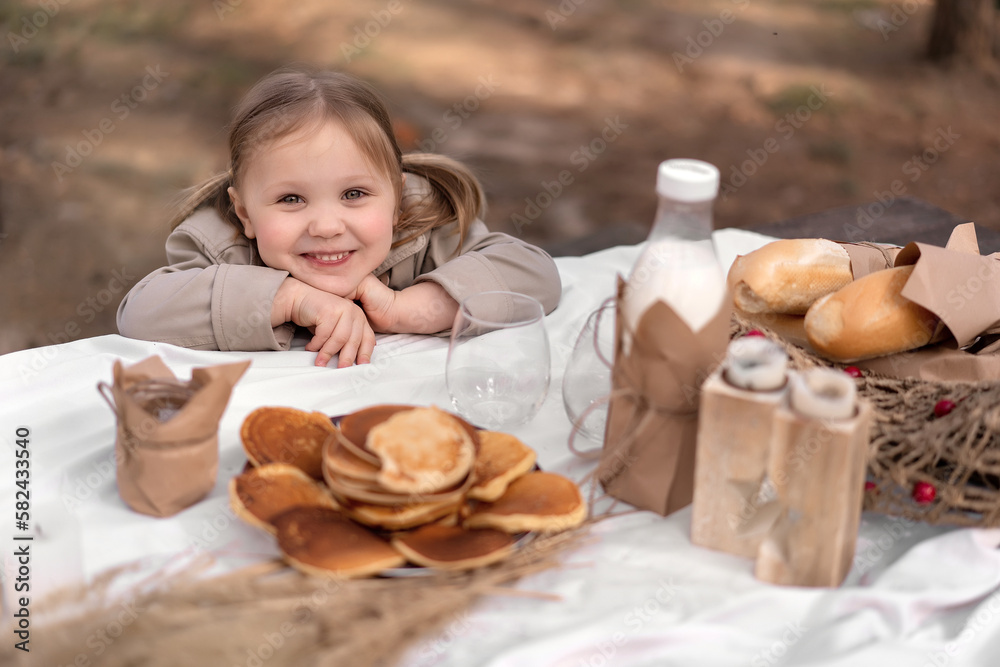 Little cute girl looking at camera and smiling sincerely, sitting at Easter table with pancakes, milk and eggs decorated in rustic style Little cute girl looking at camera and smiling sincerely, sitting at Easter table with pancakes, milk and eggs decorated in rustic style