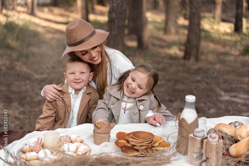 Family with children enjoying an Easter picnic in a spring garden. Mom and kids having fun outdoor lunch in spring forest, eating bread, pancakes, eggs and drinking milk in rustic style