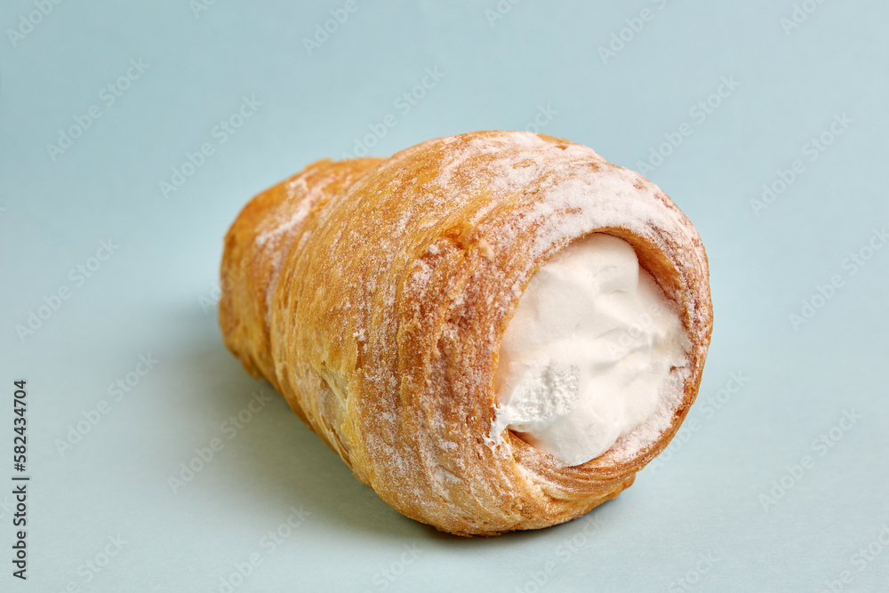 Pipe of puff pastry with meringue on a blue background.