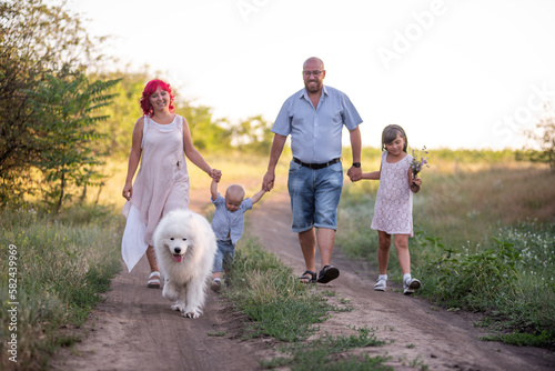 Schilderij op canvas Samoyed dog walking with bright diversity family along the paths in field summer spring