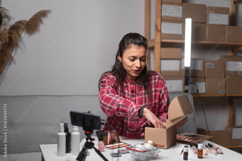 beauty influencer sitting at desk in front of cell phone set on tripod, streaming from home, promoting cosmetics, womens business concept beauty influencer sitting at desk in front of cell phone set on tripod, streaming from home, promoting cosmetics, womens business concept