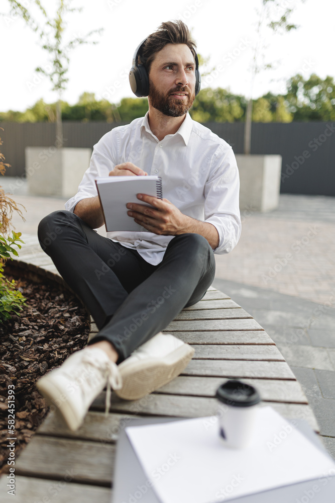 Fototapeta premium Man writing in notepad while sitting on bench with legs