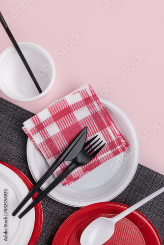 Disposable plastic tableware, cutlery and paper napkins, pink background. Vertical studio shot, close-up.