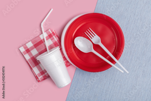 Plastic disposable tableware, cutlery on a gray napkin. Pink background, studio shot.