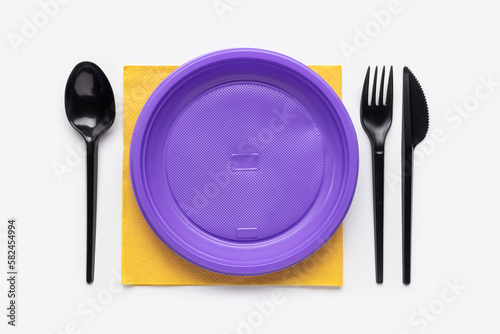 On a yellow napkin is a purple plate and cutlery. Plastic recycling. Studio shot, top view.