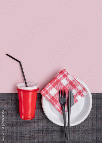 A set of plastic utensils. A glass with a straw for drinking, a plate, a napkin and cutlery.