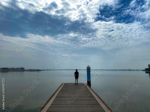 Against the background of blue sky and white clouds, an Asian woman stood on a trestle by the lake and looked up at the sky