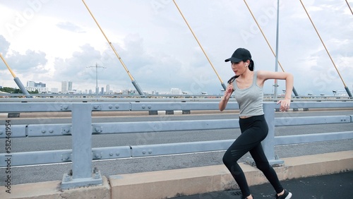 Asian woman wearing sportswear jogging on on highway bridge urban city fitness activities outdoors. Healthy lifestyle and sport concepts