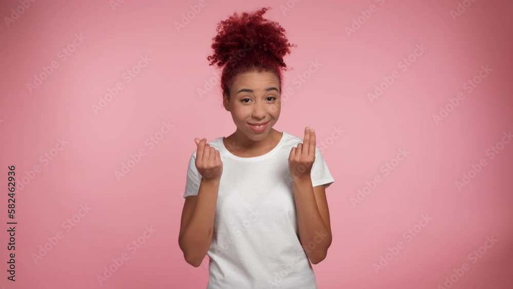 Portrait smiling African American redheaded curly woman rubbing fingers showing cash money gesture asking for give me money. Joyful female in white t-shirt looks camera on isolated pink background Portrait smiling African American redheaded curly woman rubbing fingers showing cash money gesture asking for give me money. Joyful female in white t-shirt looks camera on isolated pink background