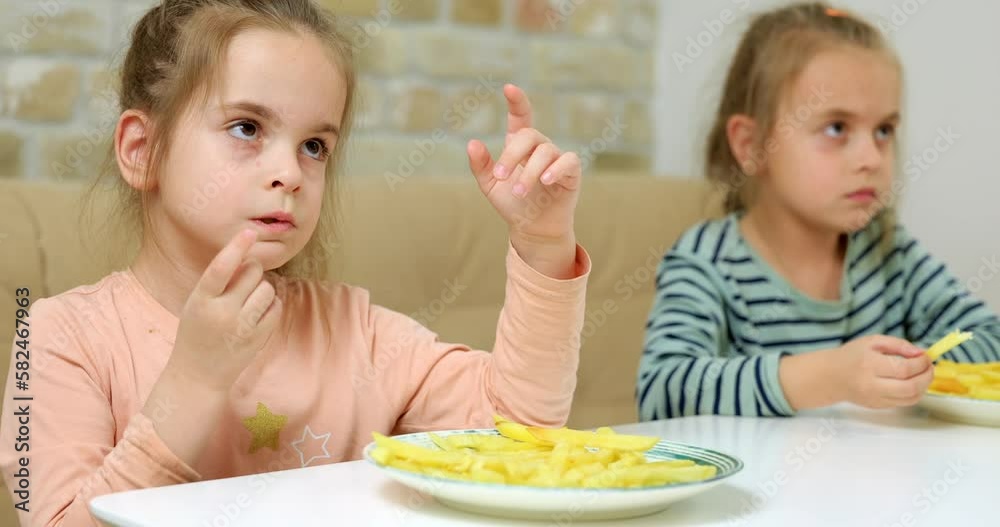 Little girls eating french fries at home and watching tv Little girls eating french fries at home and watching tv