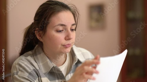 Stressed woman looking at bills and holding her head while sitting in room at home.