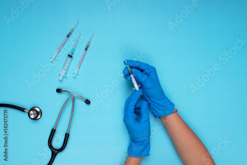 needle, stethoscope and other needles held in blue gloved hand on light blue background