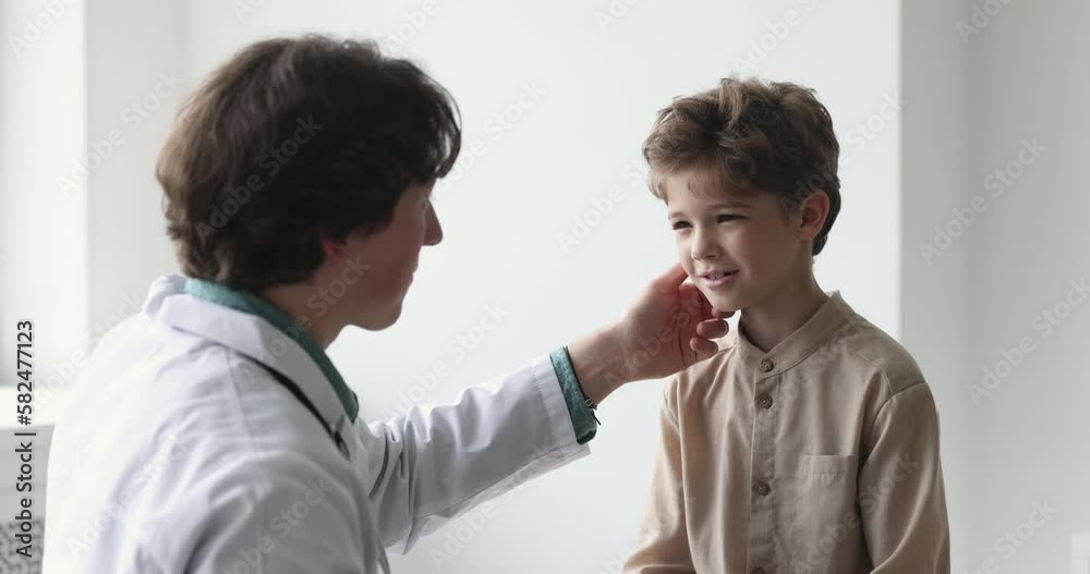 Positive caring pediatrician man examining patient child, touching lymph nodes under jaws, talking to smiling positive boy, suspecting respiratory diseases. Little kid visiting doctor in office Positive caring pediatrician man examining patient child, touching lymph nodes under jaws, talking to smiling positive boy, suspecting respiratory diseases. Little kid visiting doctor in office