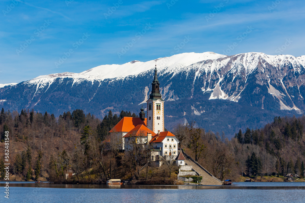 Snow capped mountain background of Lake Bled Church of the Assumption of Maria in Slovenia