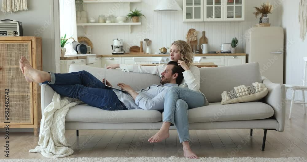 Relaxed millennial couple in love enjoying romantic leisure on home couch, using laptop computer for online communication, shopping on Internet, using application, service Relaxed millennial couple in love enjoying romantic leisure on home couch, using laptop computer for online communication, shopping on Internet, using application, service