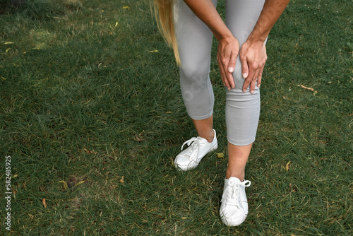 Uraz kolana. Młoda kobieta podczas treningu fitness w parku cierpi z powodu bólu kolana. Knee injury. A young woman suffers from knee pain during fitness training in the park.