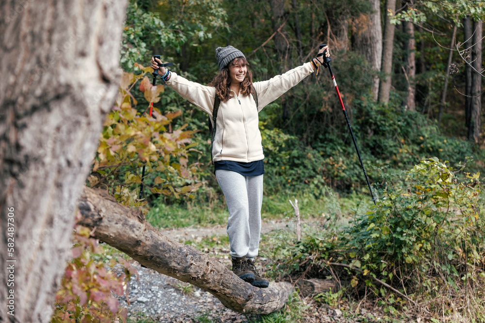 Pretty girl traveler with backpack looking to the side while walking over a log in the mountain Pretty girl traveler with backpack looking to the side while walking over a log in the mountain