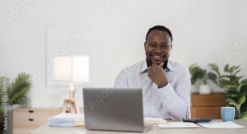 Professional male economist searches needed information on portable computer, happy to recieve high net profit, spends important banking operation. Black male trader analyzes financial market