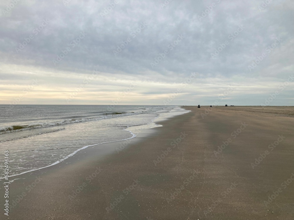 Beautiful view of calm ocean waves crashing on a deserted sandy beach on a cloudy day Beautiful view of calm ocean waves crashing on a deserted sandy beach on a cloudy day