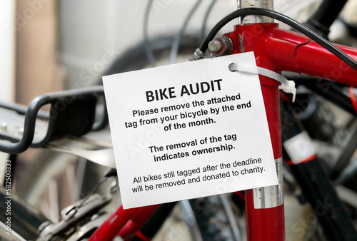 Bike audit tag attached to a bicycle with defocused bike room of strata building. Bicycle amenity audit tag with detailed instructions. Used to find unclaimed and forgotten bikes. Selective focus. photo