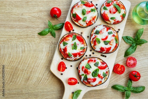 Mini eggplant pizzas-eggplants with pizza sauce,olive oil,tomatoes,mozzarella cheeses,basil and peppers on wooden pizza peel with wooden background.Healthy summer vegetarian food.Top view.Copy space