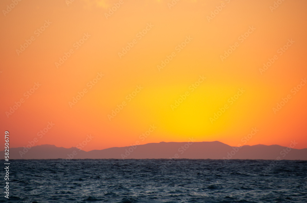 A beautiful fiery sun sets over the Mediterranean Sea on the Greek island of Paros with the blue ocean in the foreground