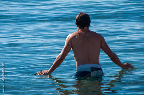 A young man stands about to swim in the blue waters of the Mediterranean Sea