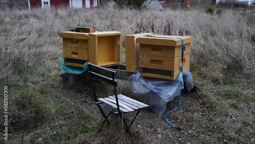 Closeup of two beehives and a small chair in a field
