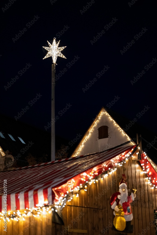 Vertical shot of a wooden house decorated with lights, a star and a Santa Claus toy on it at night