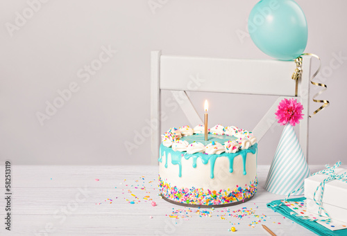 Birthday party table with vanilla cake  balloon  hat  and candle on a light grey white background