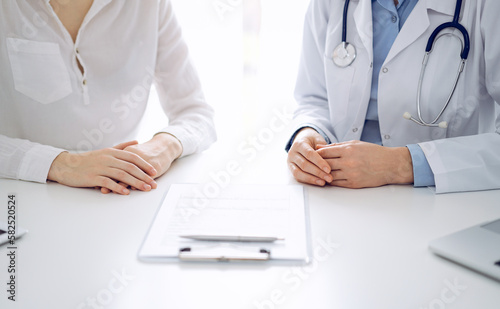 Doctor and patient discussing current health questions while sitting near of each other and using clipboard at the table in clinic  just hands closeup. Medicine concept