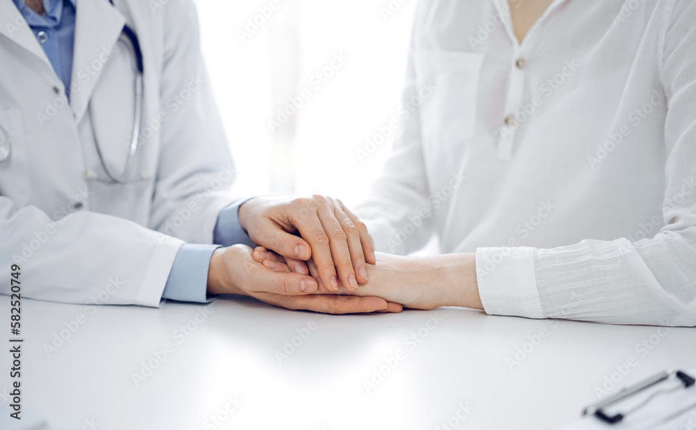 Doctor and patient sitting near each other at the table in clinic office. The focus is on female physician's hands reassuring woman, only hands, close up. Medicine concept Doctor and patient sitting near each other at the table in clinic office. The focus is on female physician's hands reassuring woman, only hands, close up. Medicine concept