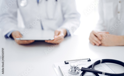 Stethoscope lying on the tablet computer in front of a doctor and patient sitting near each other and using tablet computer at the background. Medicine, healthcare concept