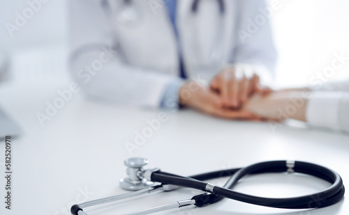 Stethoscope lying on the tablet computer in front of a doctor and patient sitting near each other. Medicine, reassuring hands concept